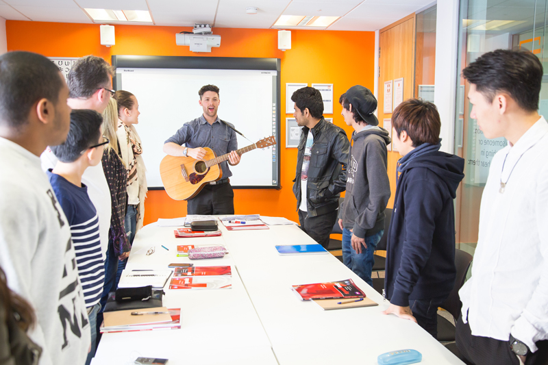 Brighton English course at EC during an English lesson while a teacher entertains students by playing the guitar